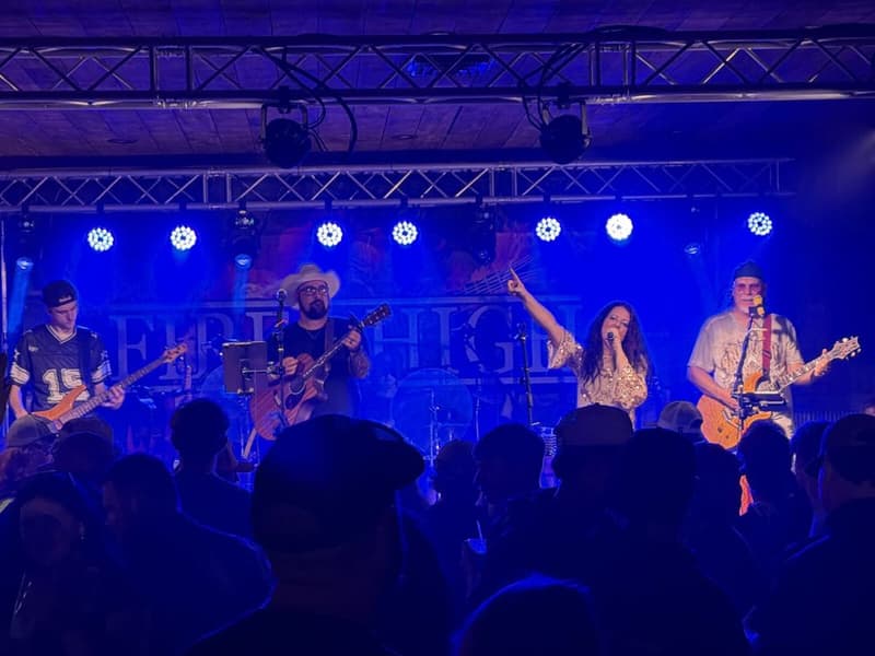 A five-piece band mid-set under blue front lighting, playing to a packed floor.