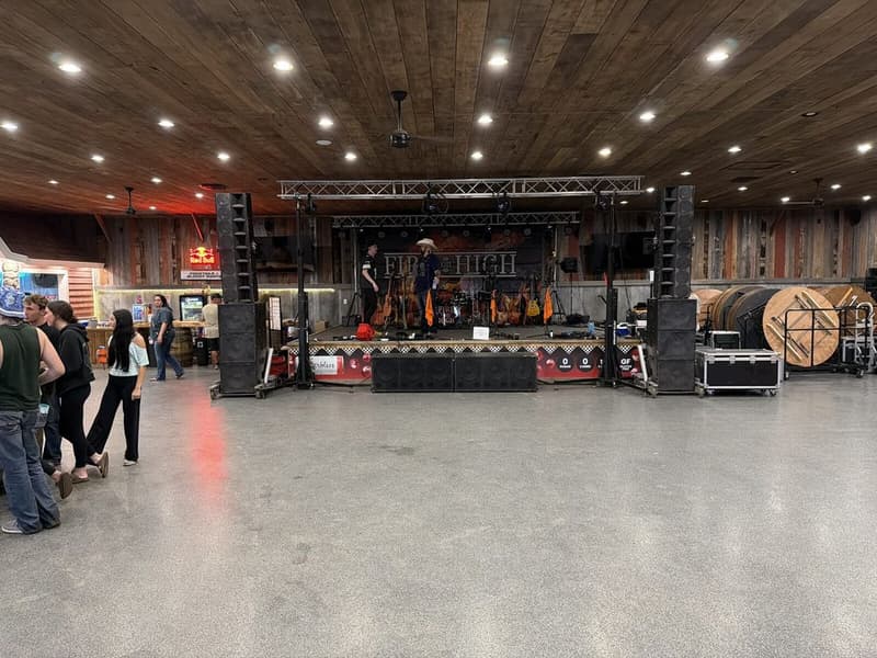 A hall before a show: PA cabinets flown either side, subwoofers across the front, and a lighting truss over an empty floor.